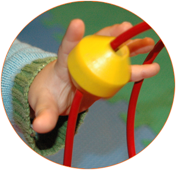 Nahaufnahme einer kleinen Kinderhand, die eine gelbe Kugel durch eine rote Motorikschleife führt. Das Foto entstand in einer Krabbelgruppe von Tüpfelhausen und steht für die spielerische Förderung der frühkindlichen Entwicklung.