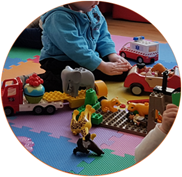 Nahaufnahme einer kleinen Kinderhand, die eine gelbe Kugel durch eine rote Motorikschleife führt. Das Foto entstand in einer Krabbelgruppe von Tüpfelhausen und steht für die spielerische Förderung der frühkindlichen Entwicklung.